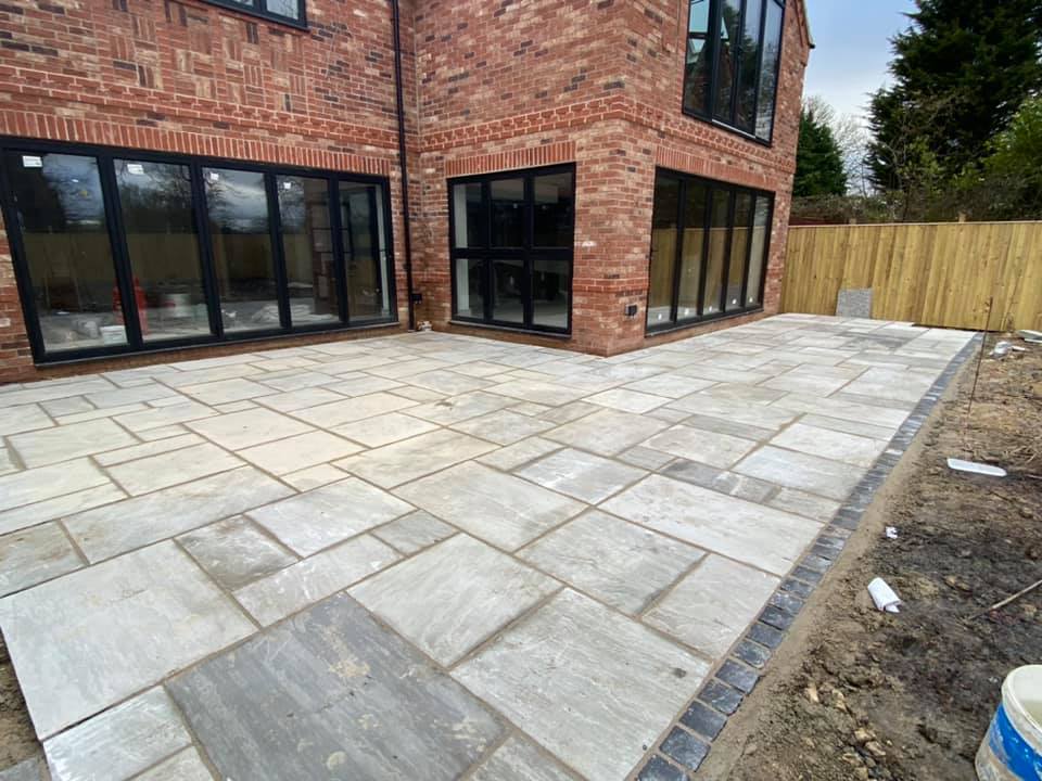 A newly laid sandstone patio behind a red brick house