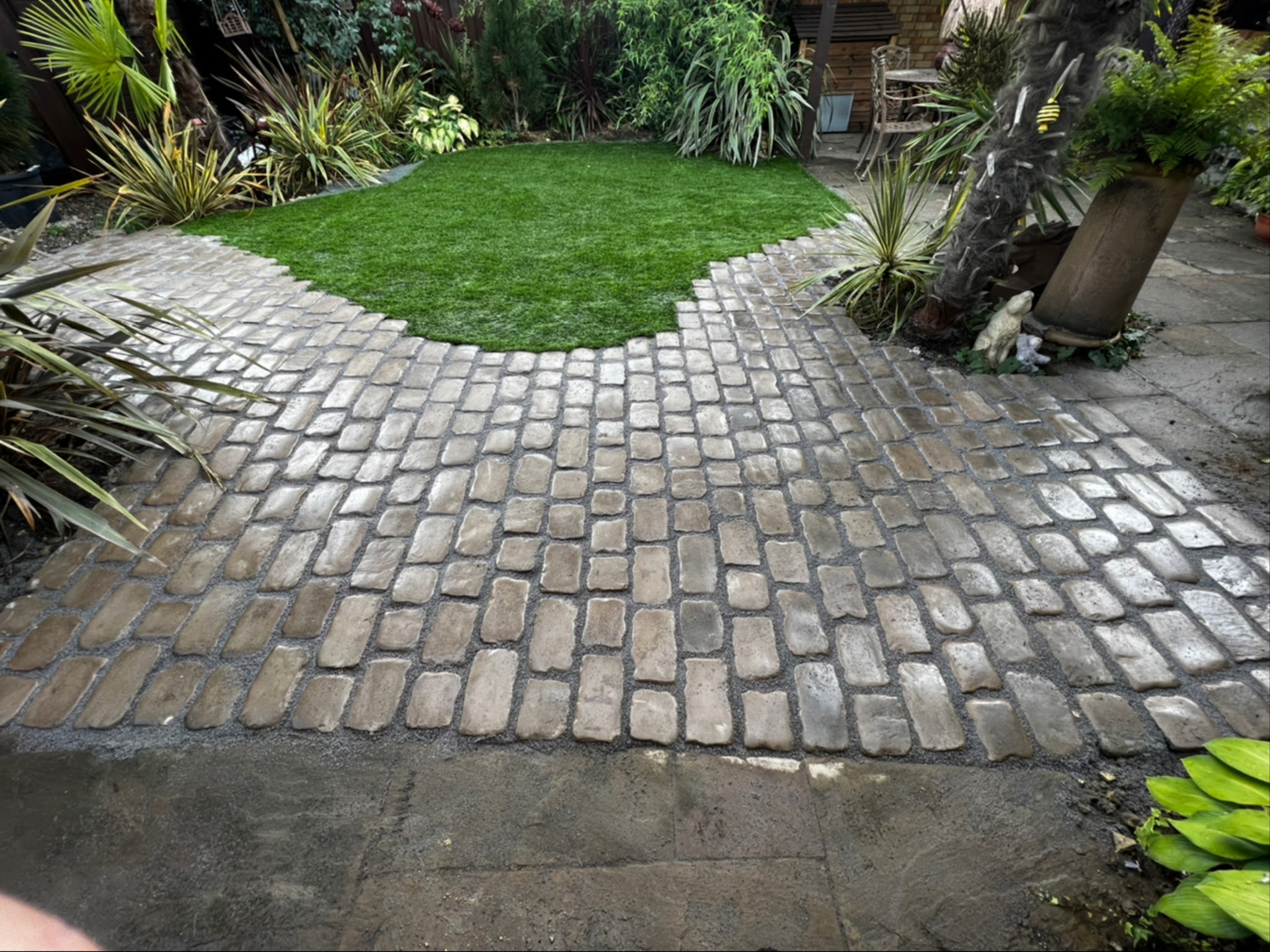 Curved cobbled path laid around a lawn with tropical planting