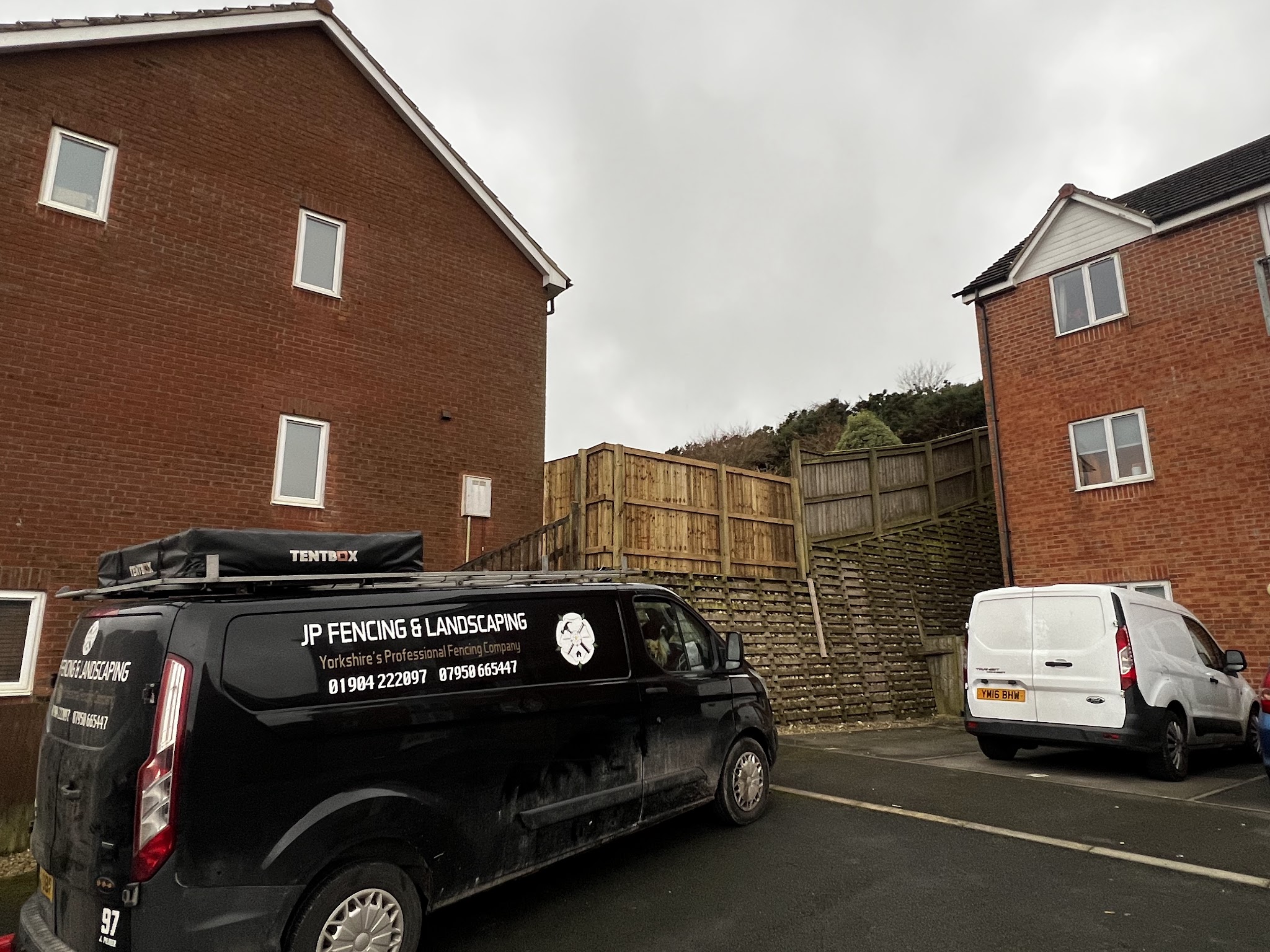 The JP Fencing & Landscaping van parked below a new fence on a retaining wall