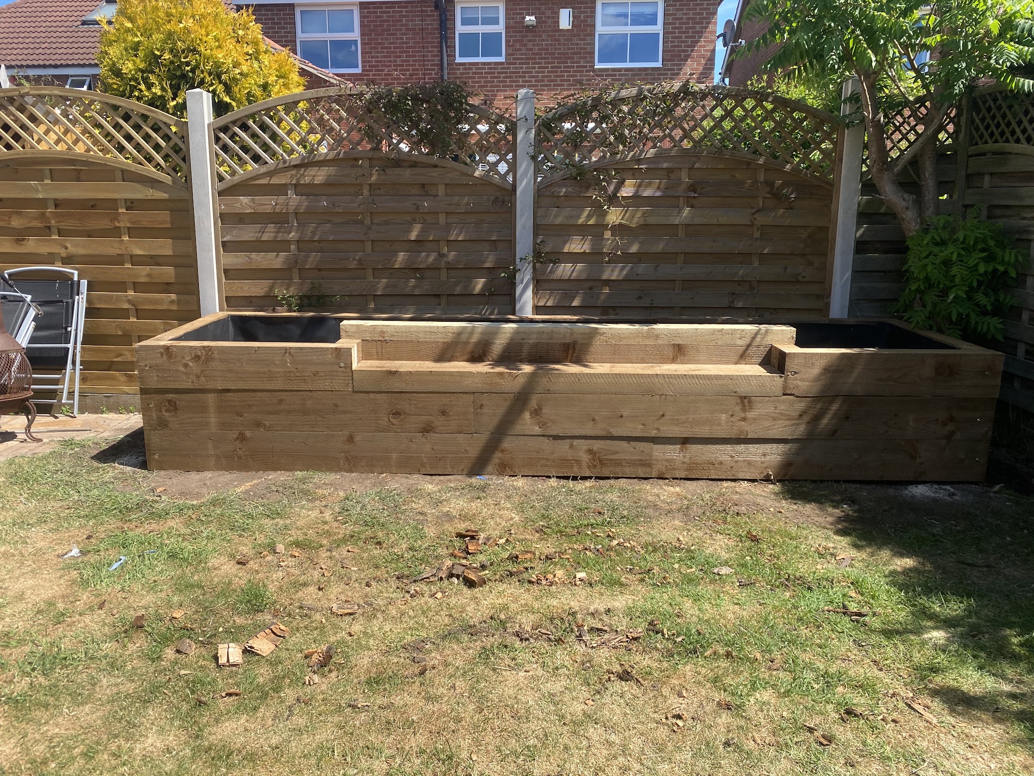 Raised timber sleeper beds built in front of a garden fence